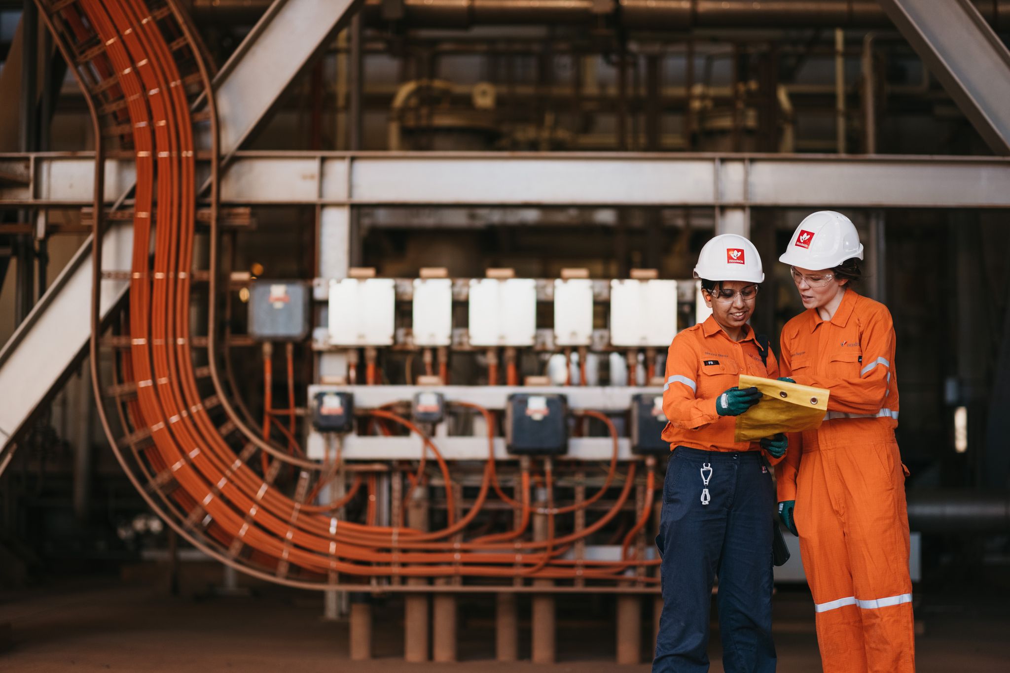 Two Woodside employees discussing in front of large pipes and equipment at Woodside's Scarborough Gas Plant