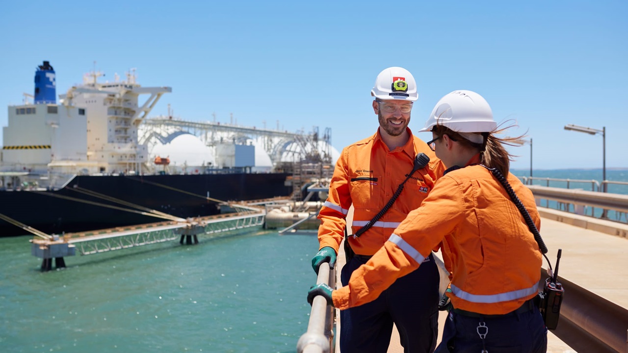 Two Woodside employees chatting on a platform in front of a large ship