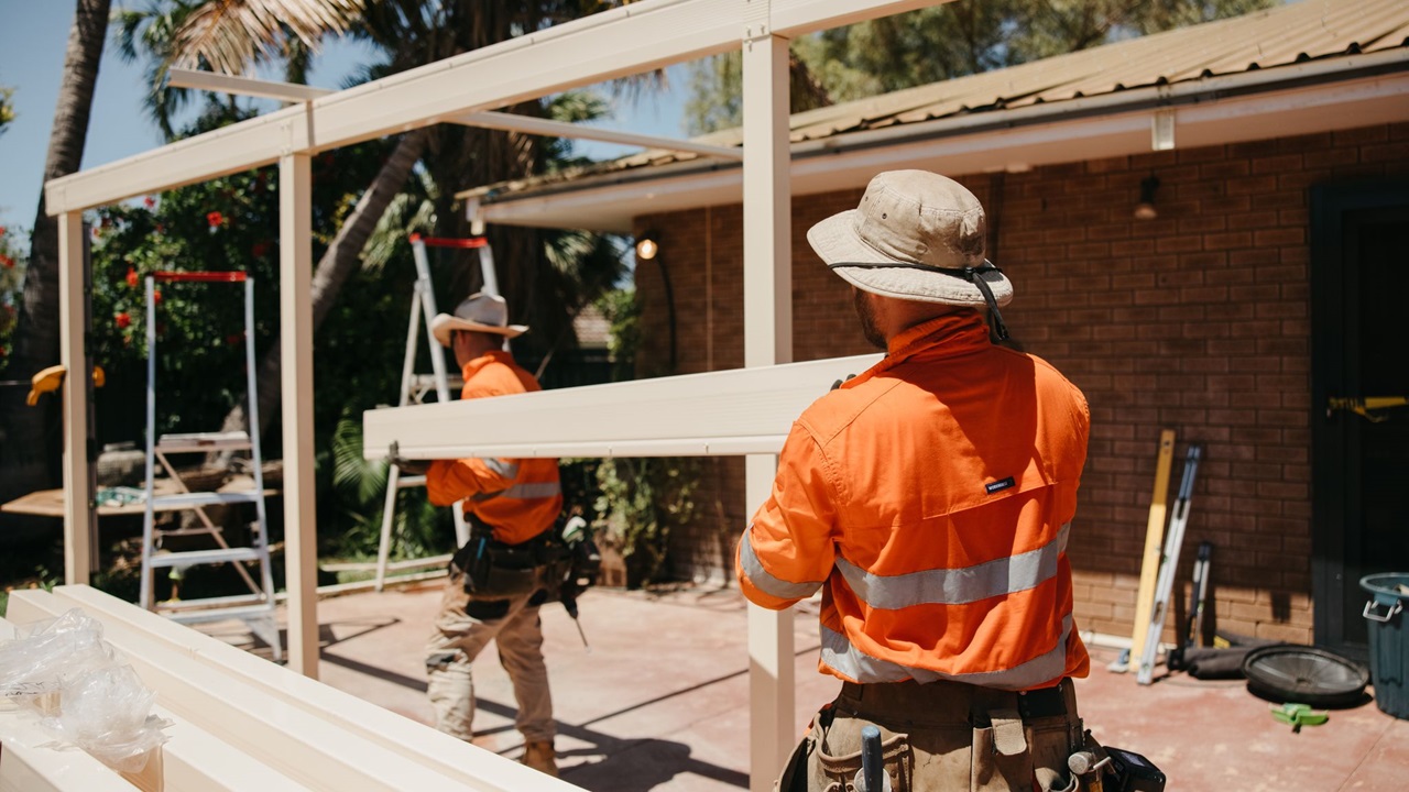 Two Woodside employees on a house construction site carrying a large beam