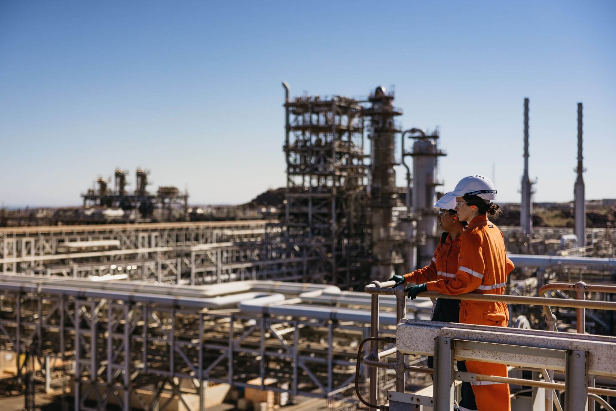 Two Woodside employees standing on a metal platform overlooking the Scarborough Gas Plant